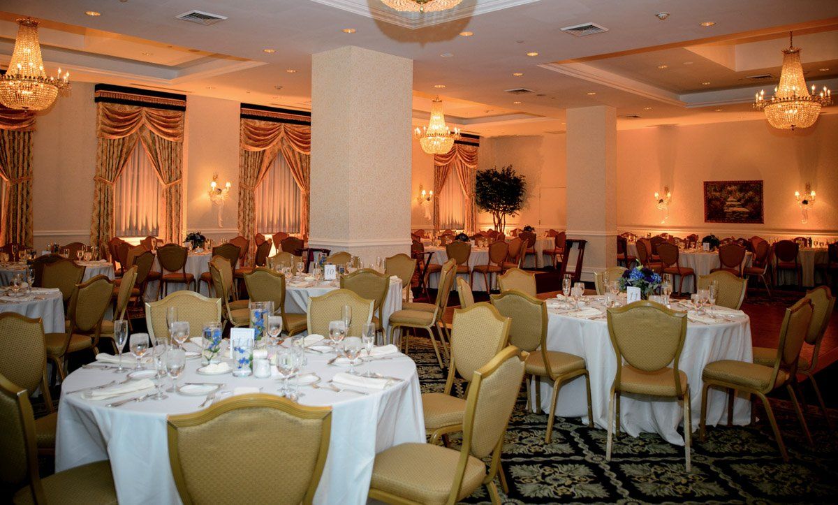 Formal banquet hall, round tables with white tablecloths, gold chairs, ornate chandeliers, warm lighting.