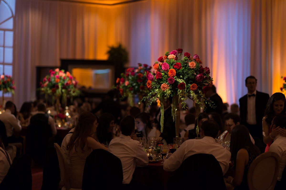 Elegant reception: floral centerpieces, people dining at tables, and warm lighting.