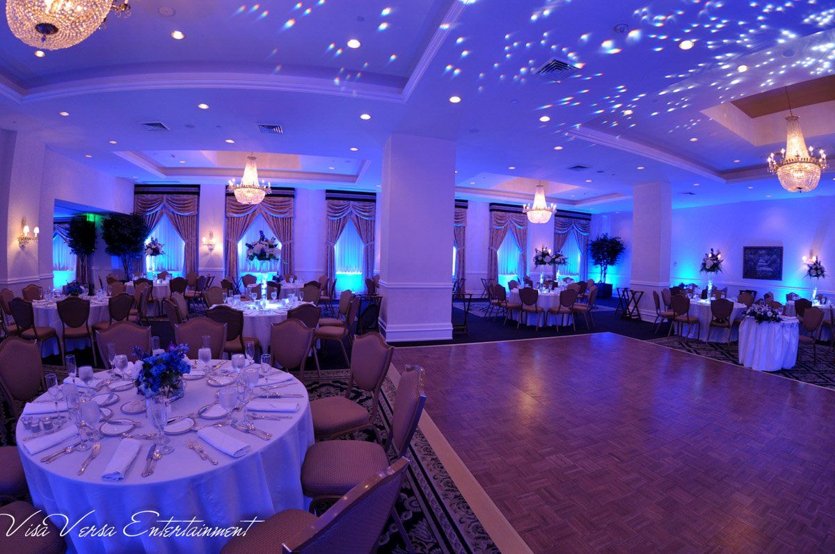 Blue-lit banquet hall with round tables set for a formal event; chandeliers and starry ceiling projection.