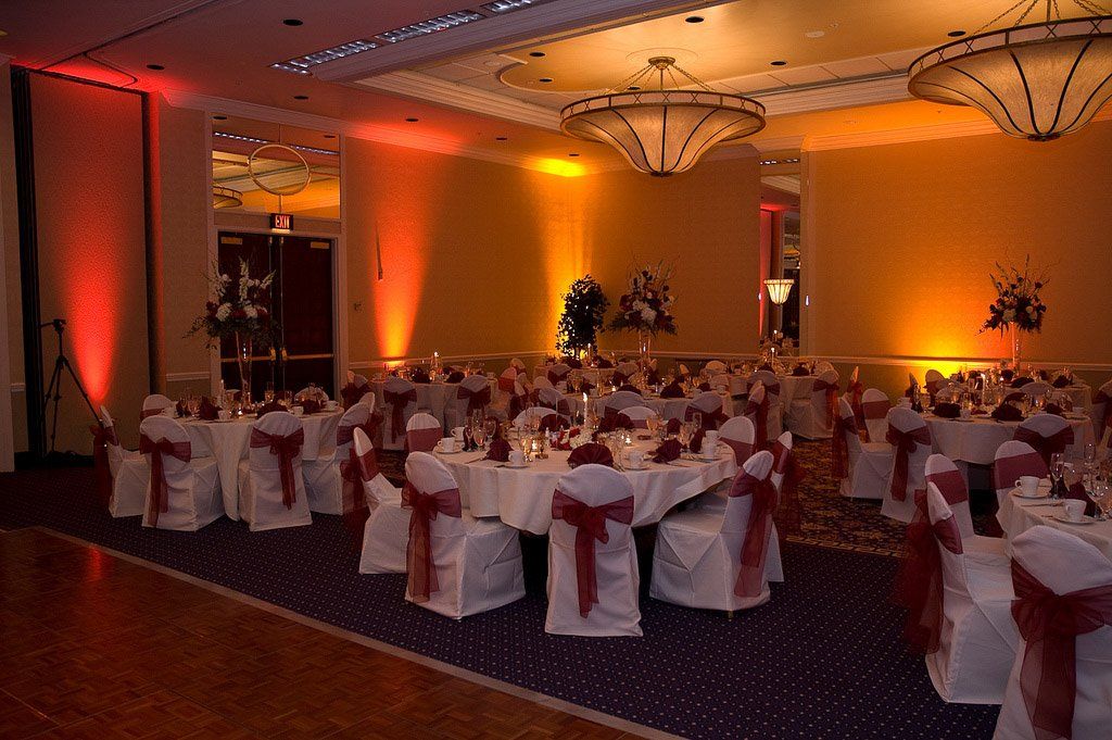 A banquet hall set for a wedding with round tables, white linens, red accents, and warm lighting.