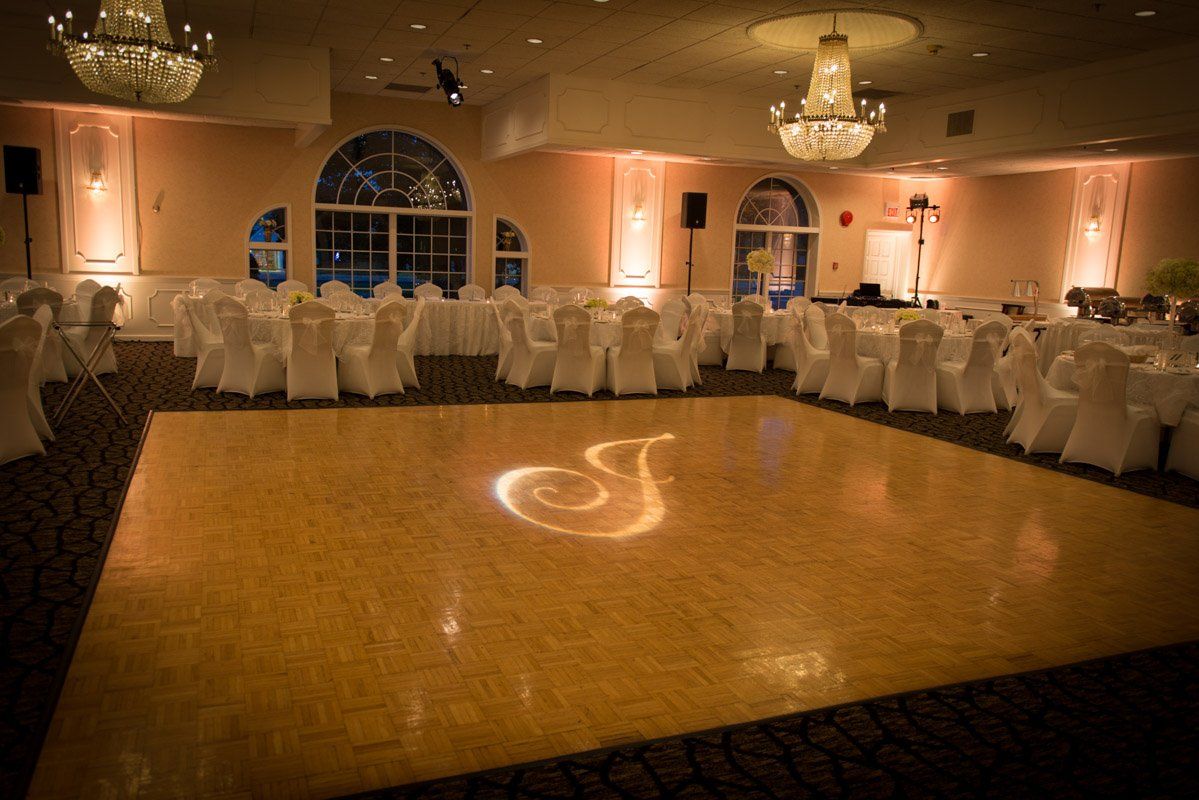 Empty ballroom with a lit dance floor, tables set for a party, and chandeliers.