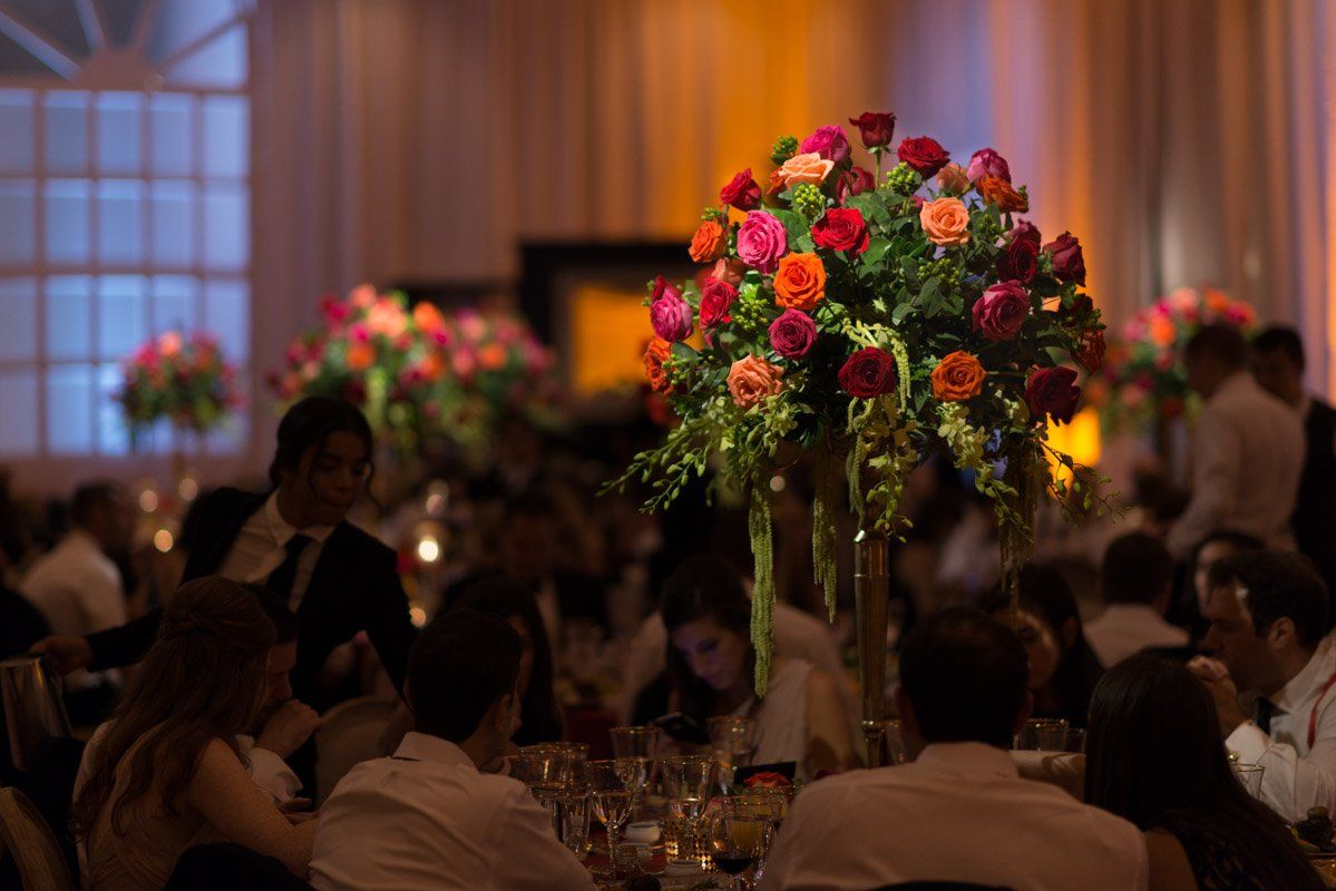 Elegant event with floral centerpieces, people seated at tables, soft lighting.