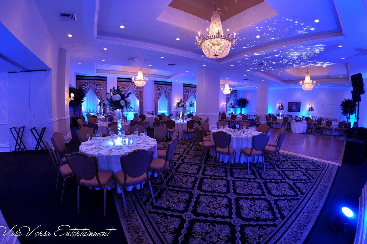 Elegant ballroom with round tables, blue lighting, chandeliers, and a star-like ceiling effect.