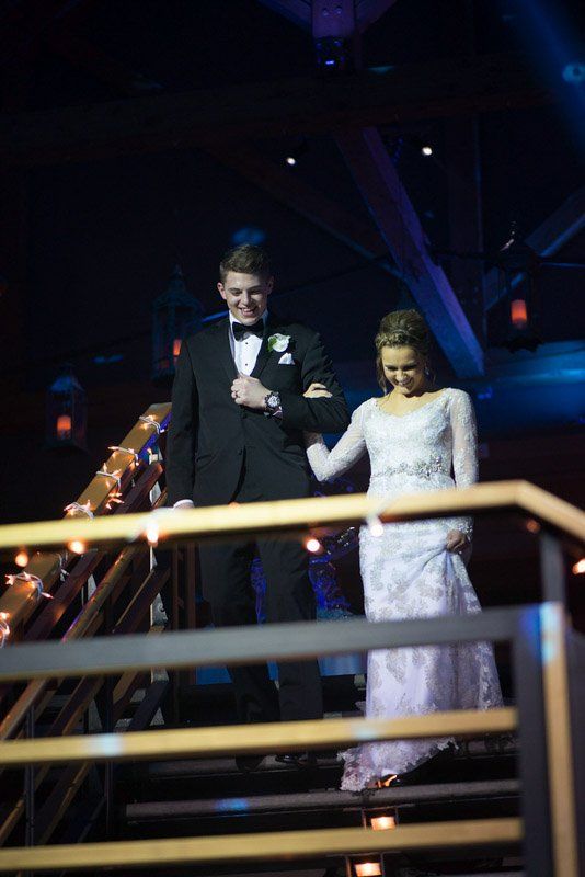 A young couple descends stairs at a formal event. The man in a tuxedo, the woman in a white gown.