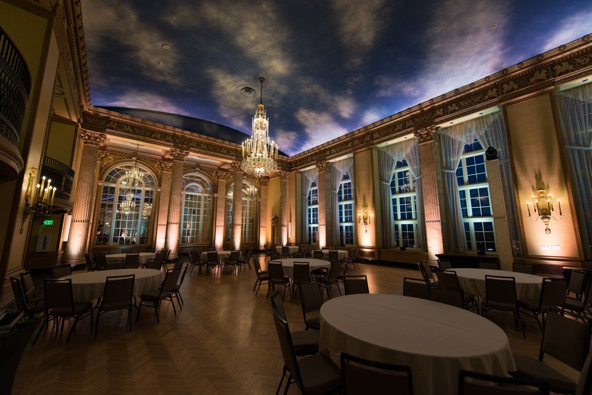 Elegant ballroom with round tables, ornate architecture, and a sky-painted ceiling.