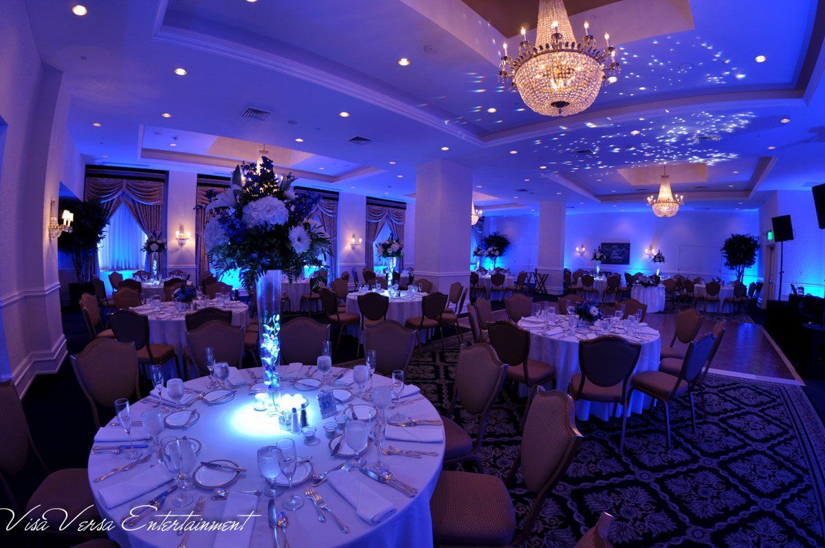 Elegant banquet hall with round tables, blue lighting, and crystal chandeliers.