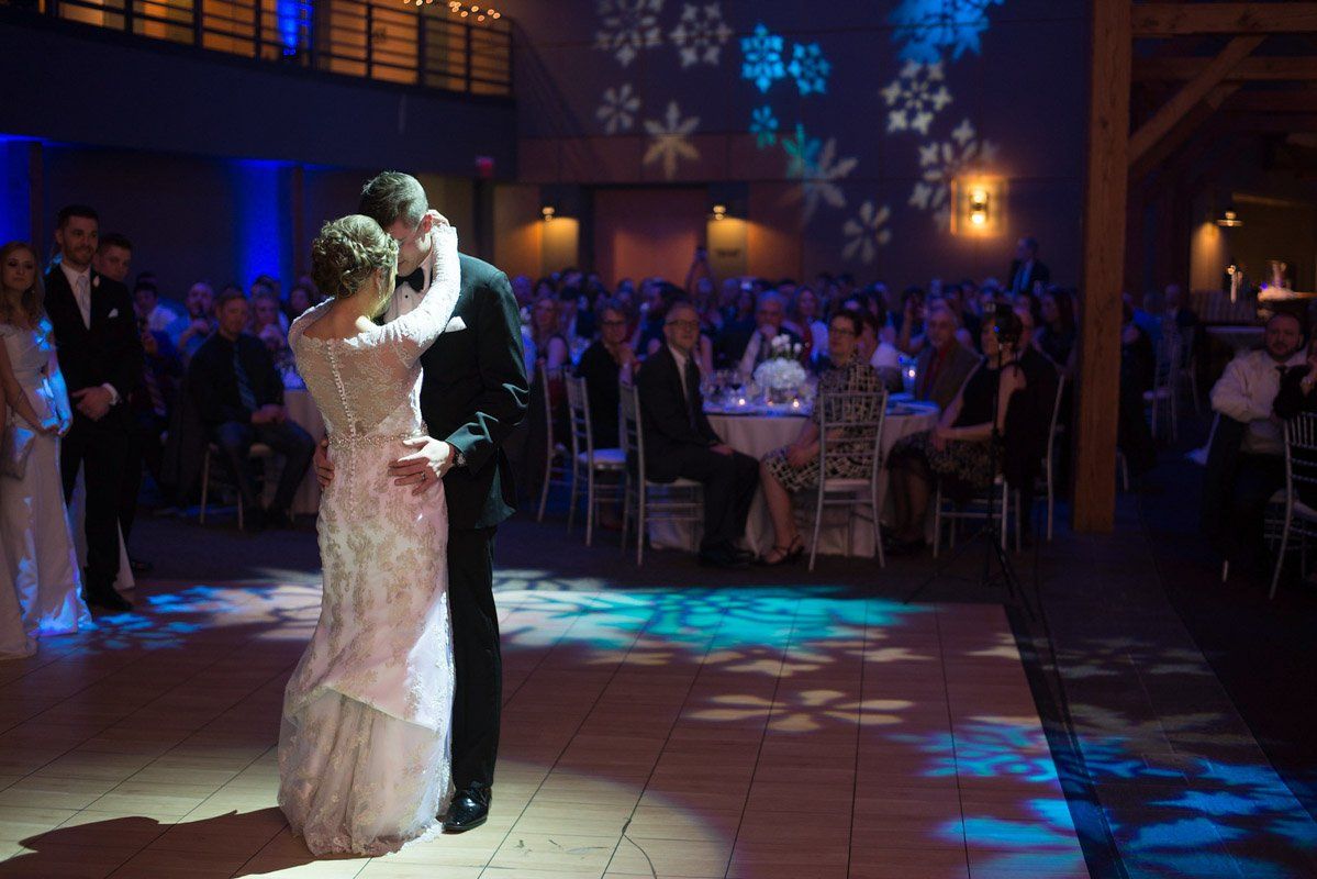 Bride and groom dance at wedding reception, surrounded by guests and snowflake projections.