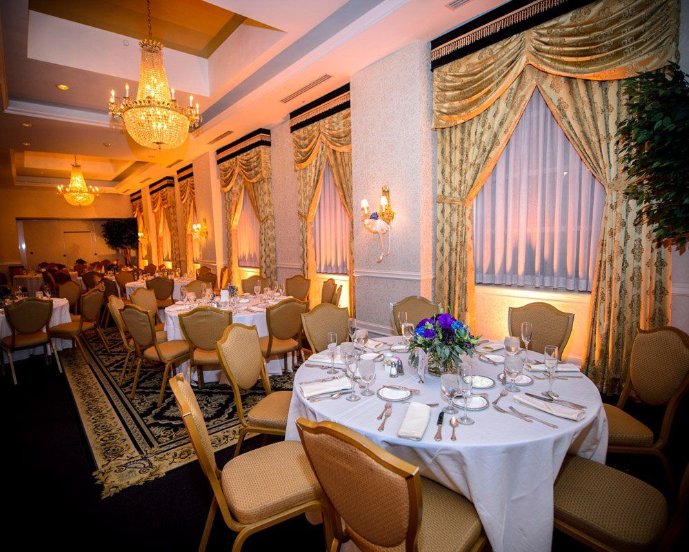 Elegant banquet hall with round tables set for dinner, gold chairs, chandeliers, and ornate curtains.