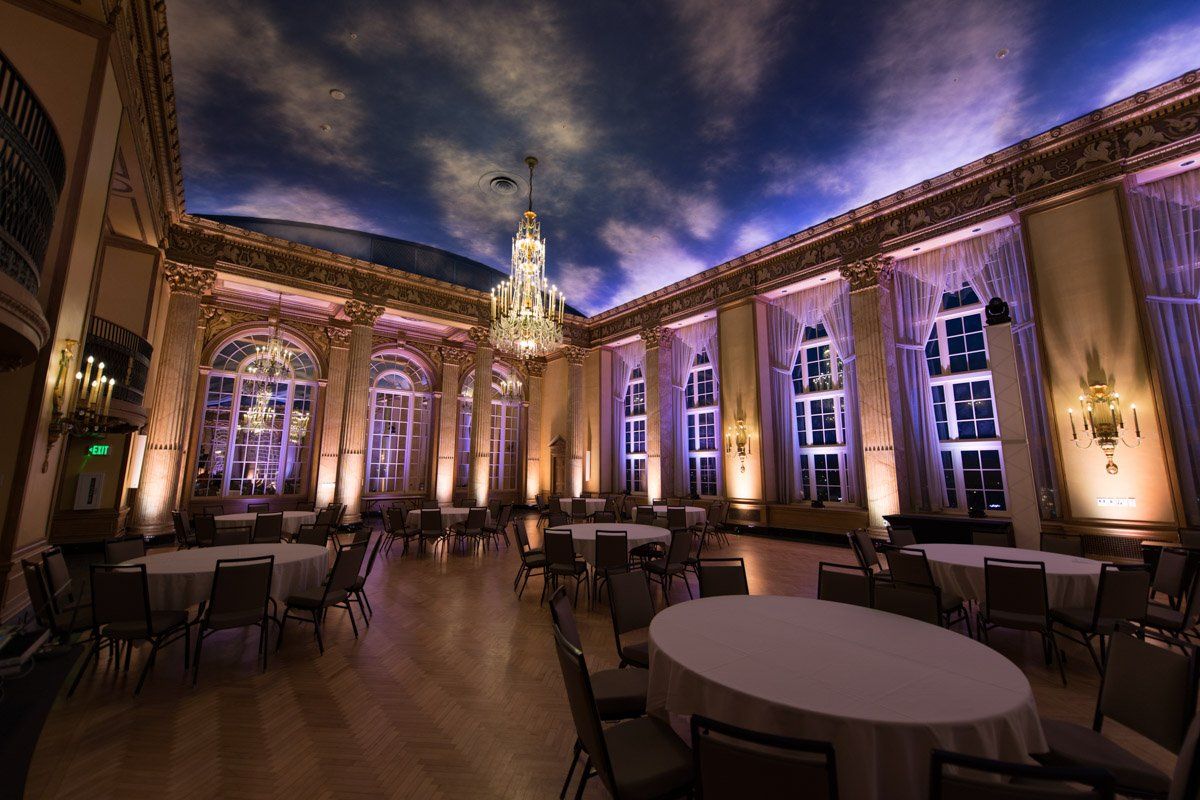 Elegant ballroom with round tables, chandeliers, and painted sky ceiling.