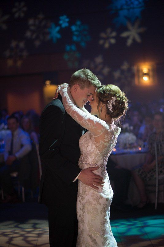 Couple dancing at a wedding reception; woman in white dress, man in black suit, snowflakes projected above.
