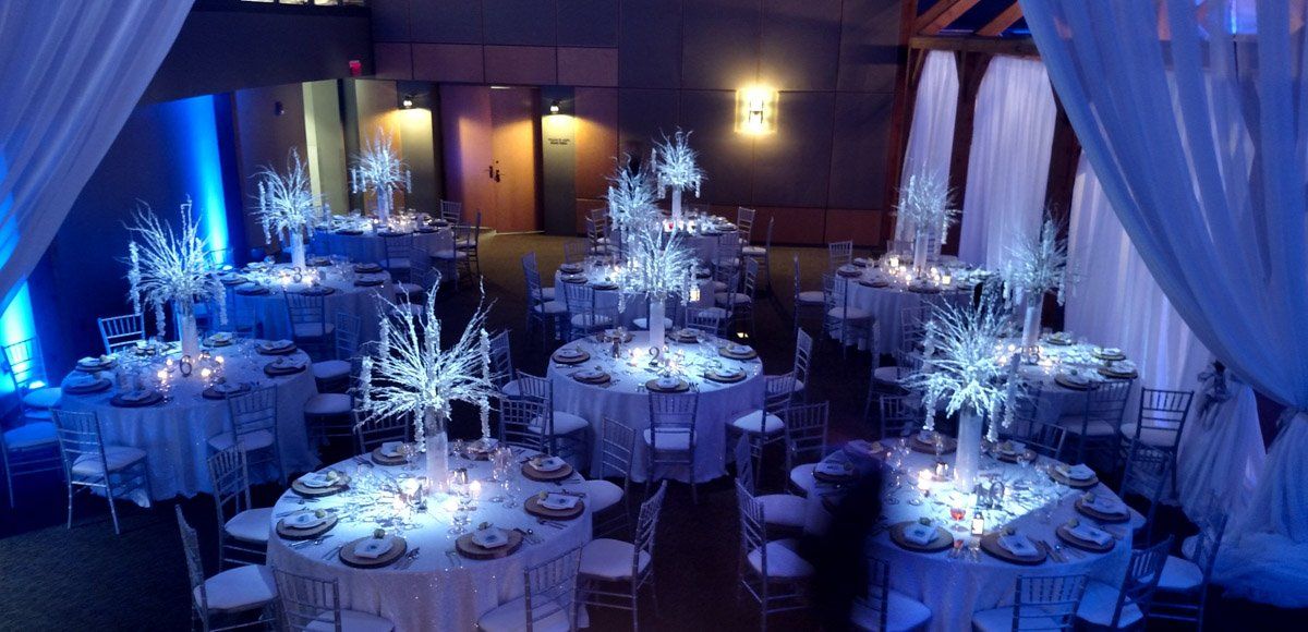 Elegant banquet hall with round tables decorated in white and blue for a wintery event.