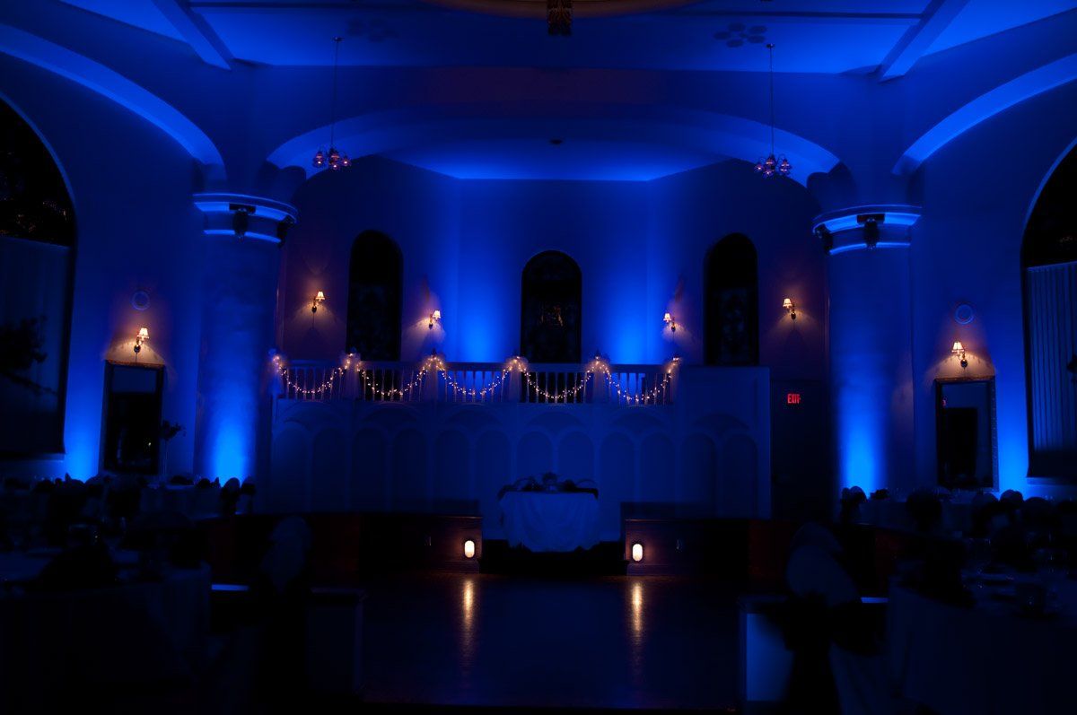 A dimly lit event space bathed in blue light, featuring a stage, decorations, and seated guests.