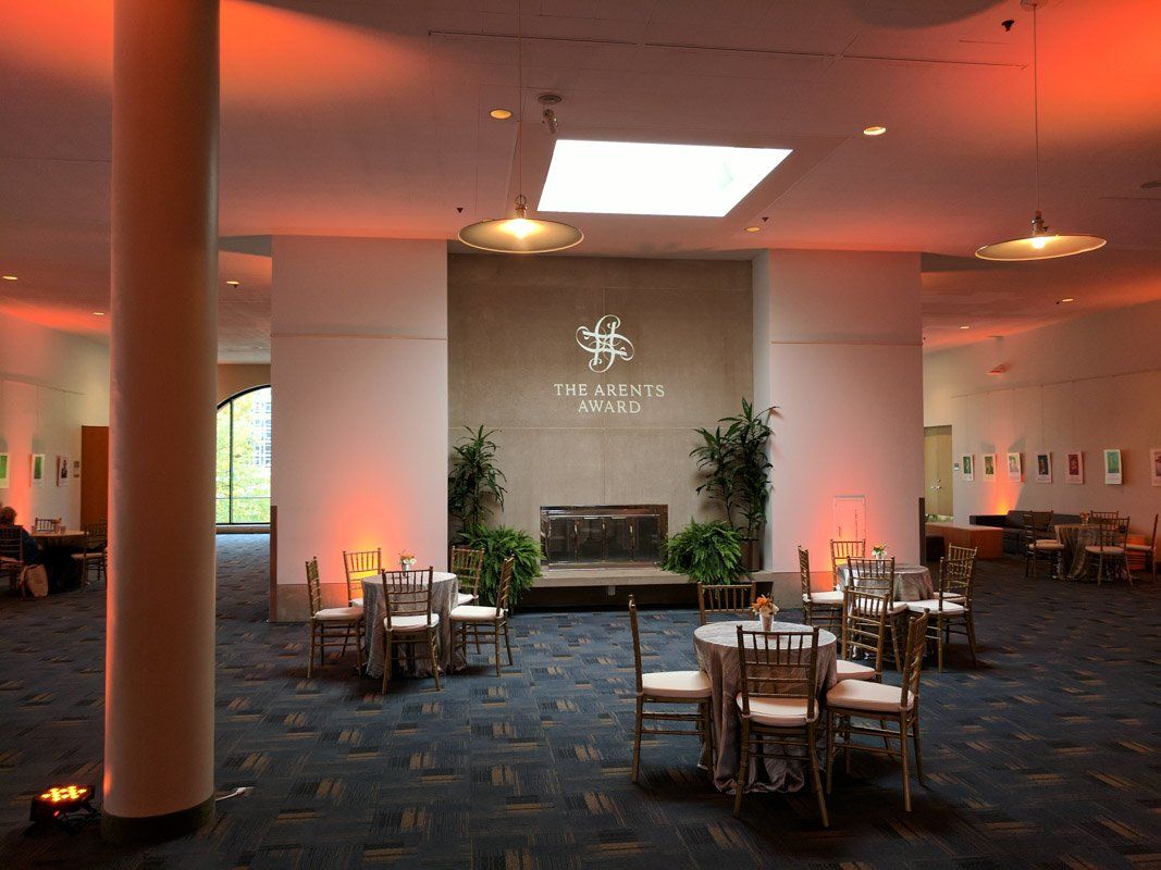 Elegant event space with tables, chairs, fireplace, and warm lighting; logo on wall.