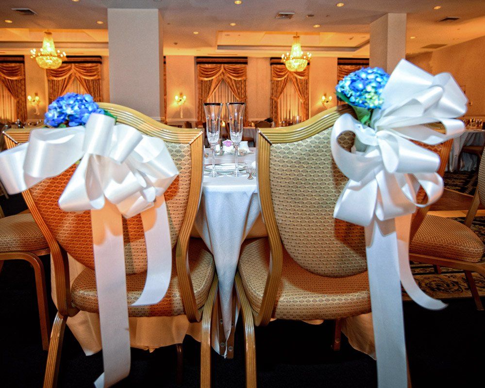 Wedding reception chairs with white bows, blue flowers, and champagne glasses.