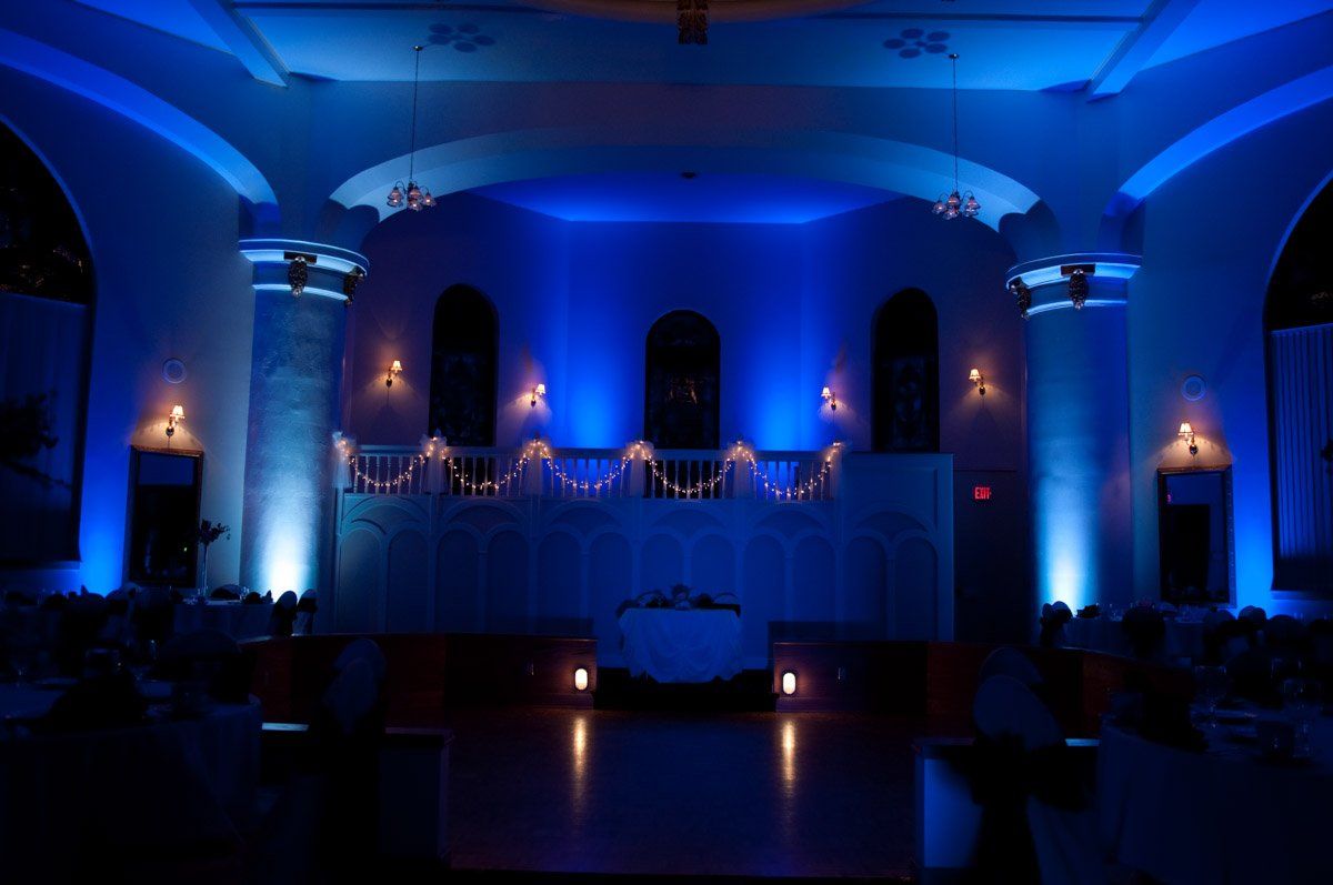 Ceremony hall lit with blue uplighting.  Stage has white accents.