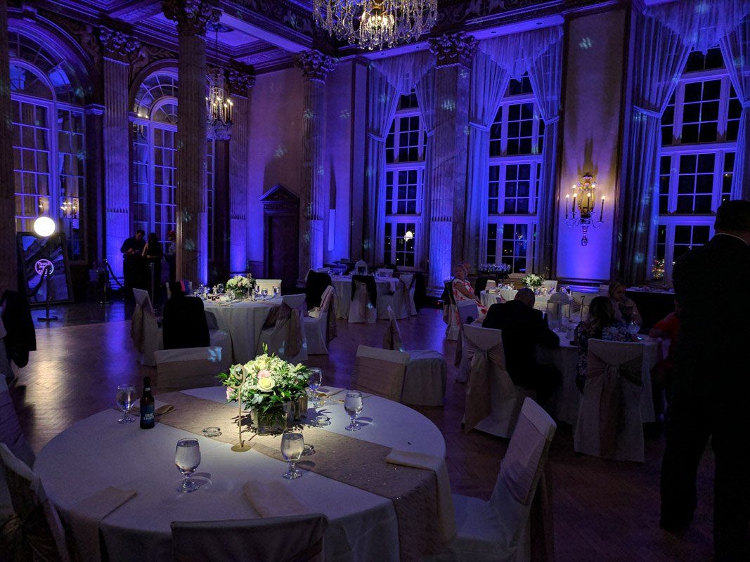 A wedding reception hall lit with blue lights, featuring round tables with centerpieces and guests.