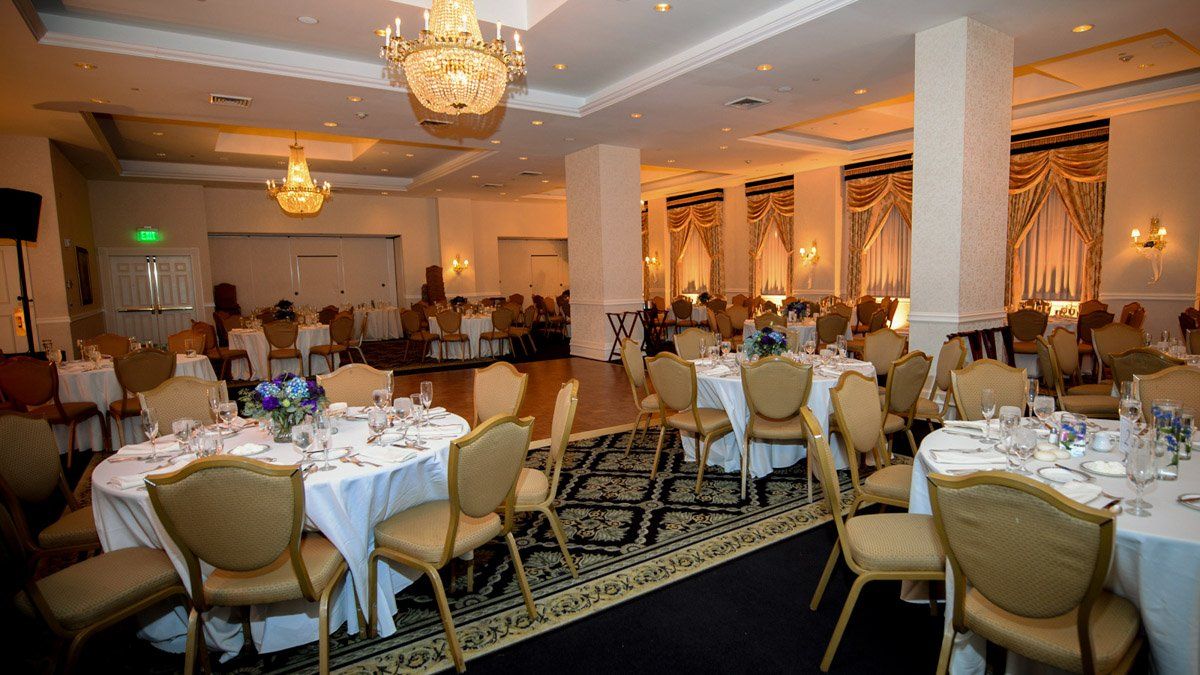 A banquet hall with round tables set for a formal event, golden chairs, and chandeliers.