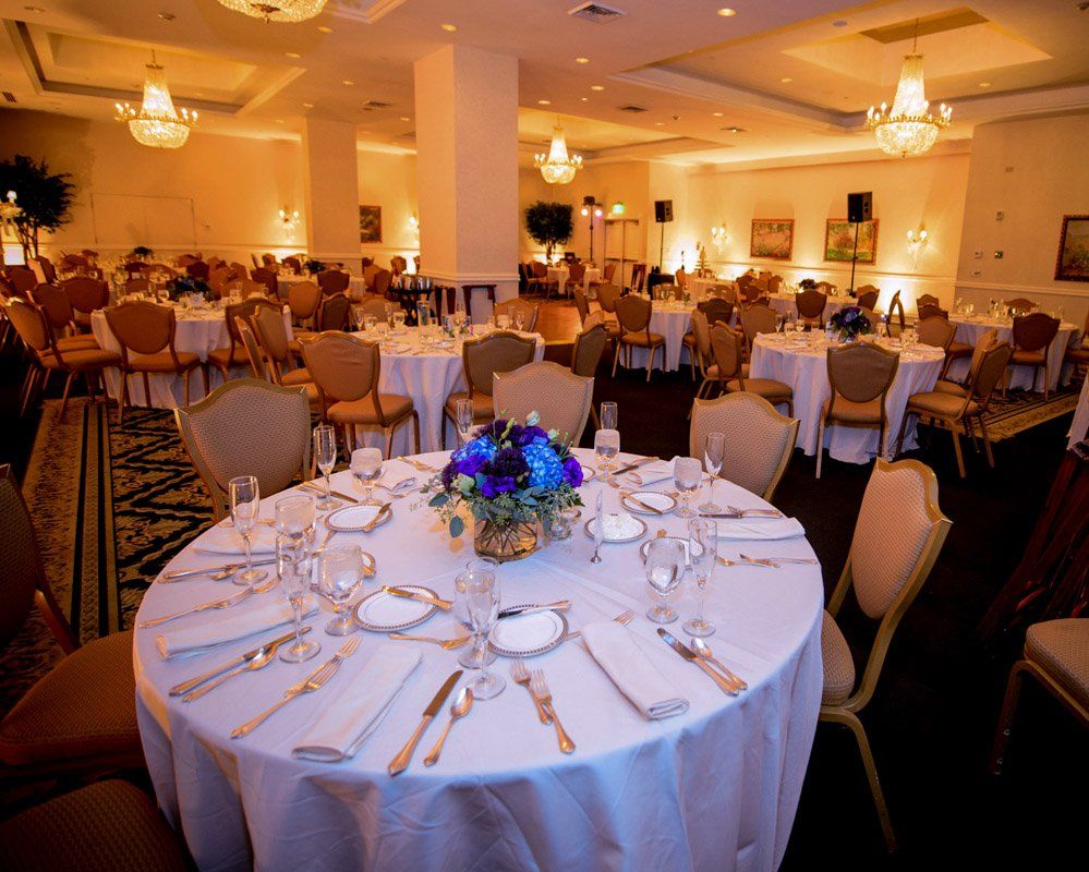 Elegant ballroom with round tables set for dining, ornate chairs, floral centerpieces, and chandeliers.