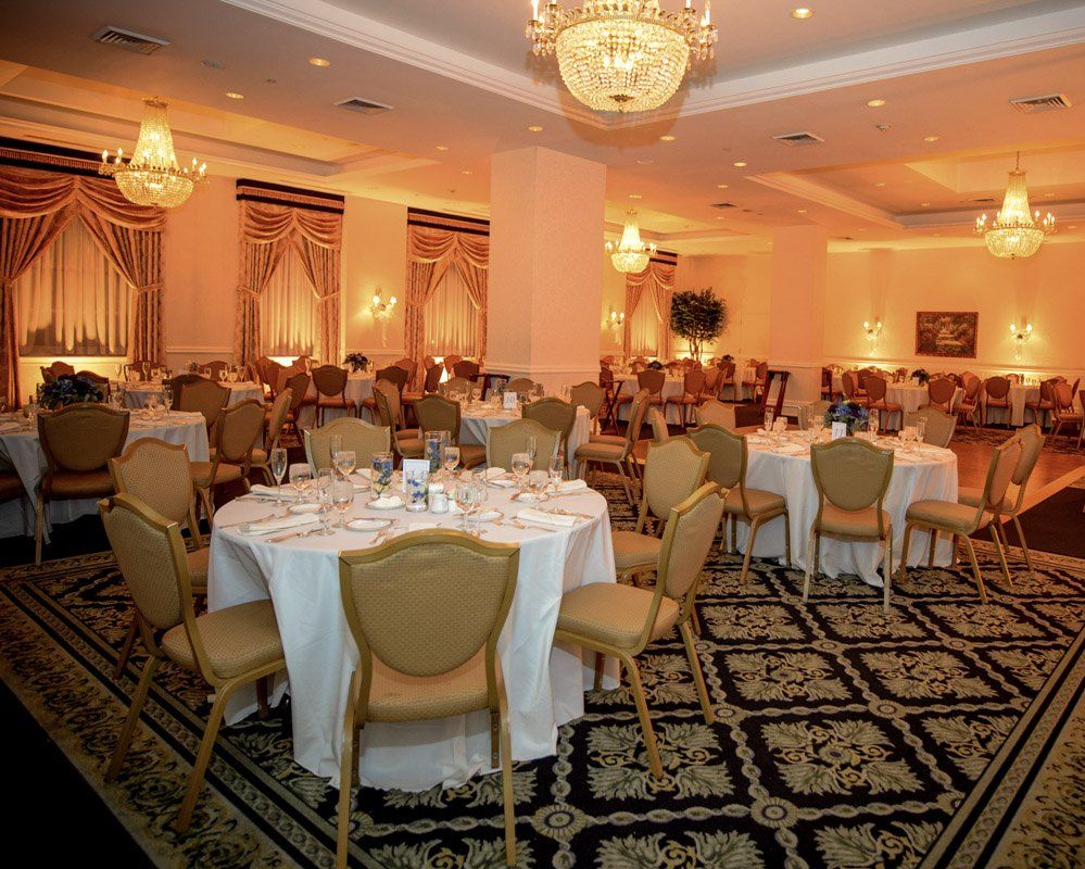 Elegant banquet hall, round tables set for dining, chandeliers, ornate gold chairs, patterned carpet.
