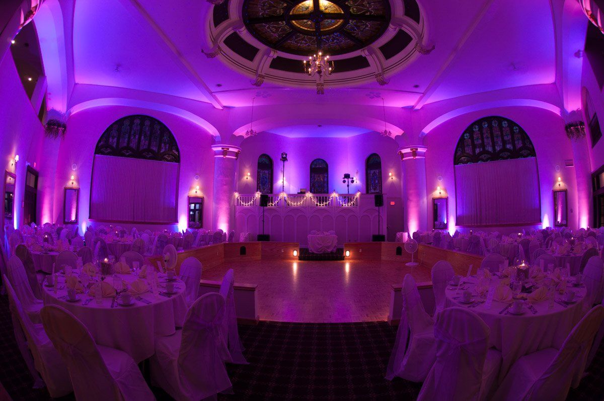 Elegant ballroom with purple up-lighting, tables set for a formal event, and a dance floor.