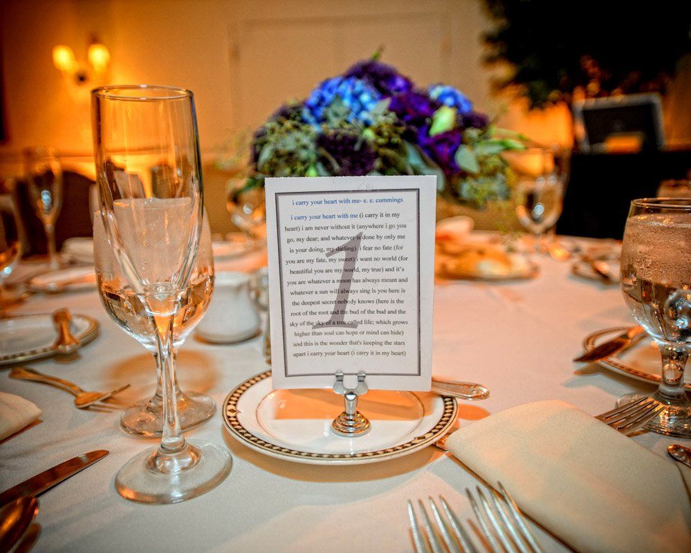 Close-up of a table setting with a table number, flower arrangement, and glasses, suggesting a formal event.