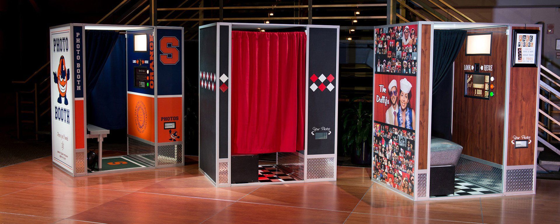Three photo booths decorated with orange, blue, and wood paneling in a dimly lit room.