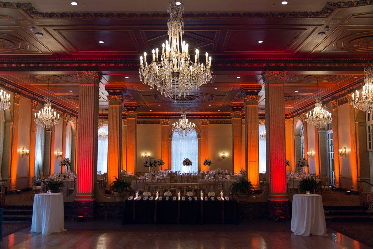 Elegant ballroom with chandeliers, orange uplighting, and a decorated head table.