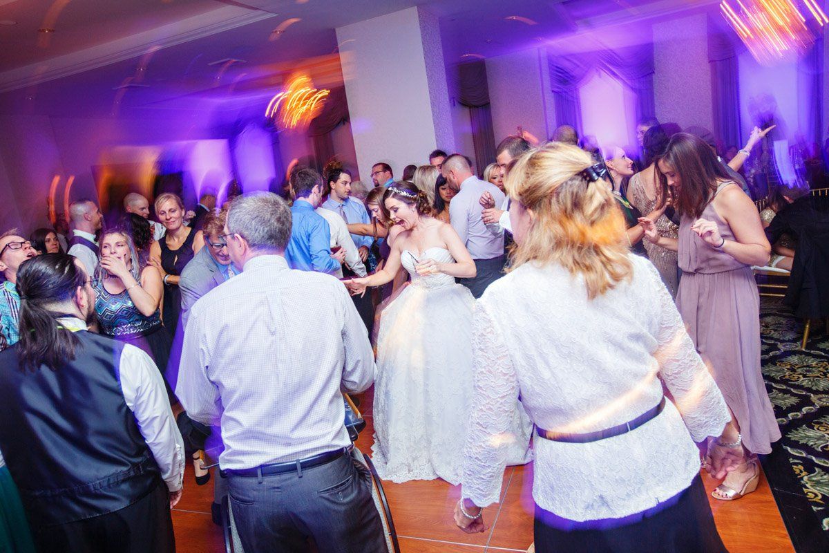 Wedding reception dance floor with bride and guests dancing under purple lights.