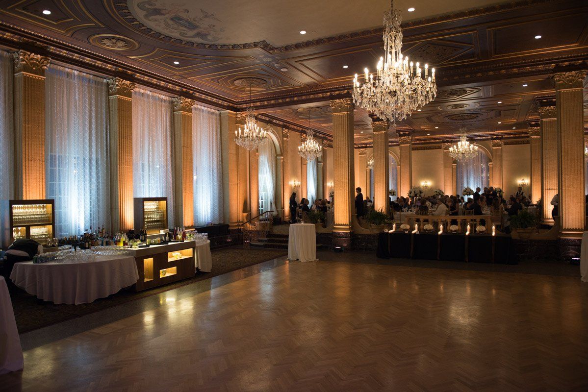 Elegant ballroom with chandeliers, tables set, and guests in attendance. Warm lighting and high ceilings.