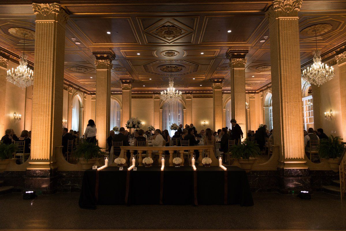 Elegant ballroom lit with golden light, guests gathered.  Central focus on a draped stage, ornate columns.