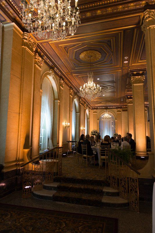 Formal dining room with ornate architecture, chandeliers, and a seated dinner.