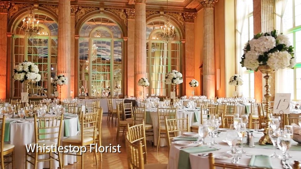 Elegant ballroom with round tables, gold chairs, and white floral centerpieces.
