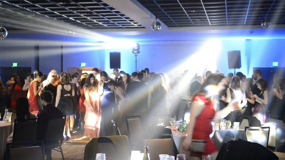 People dancing at an event in a brightly lit ballroom, illuminated by spotlights and blue lights.