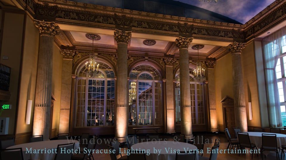 Elegant ballroom lit in amber and violet, with tall windows and ornate columns. Syracuse Marriott Hotel.