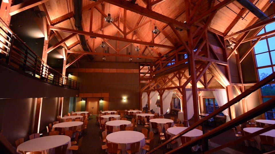 Banquet hall with wooden beams, round tables, warm lighting.
