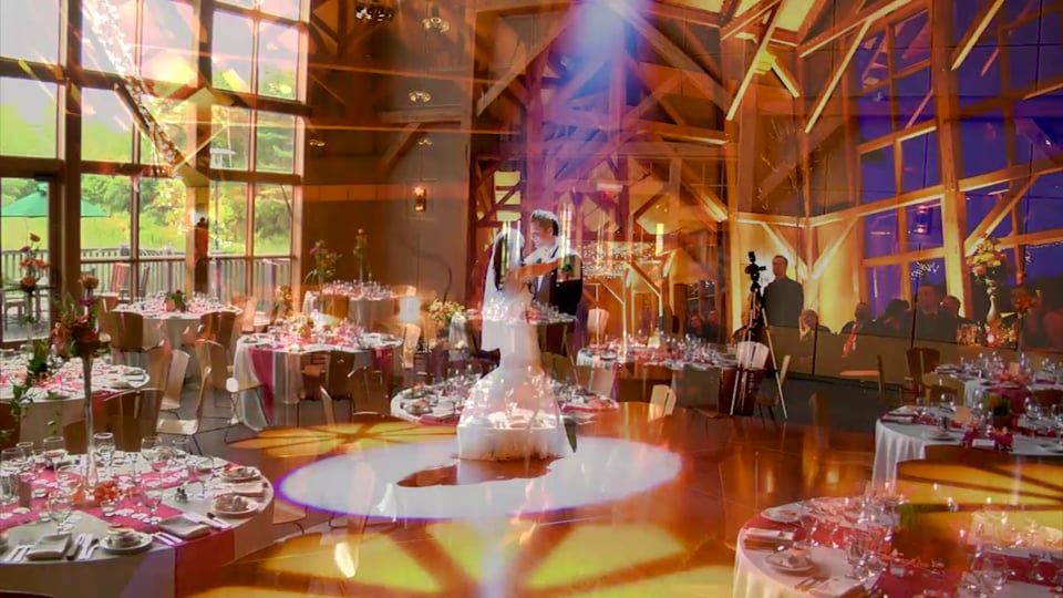 Bride and groom dance on a lit dance floor at a wedding reception in a venue with tables and large windows.