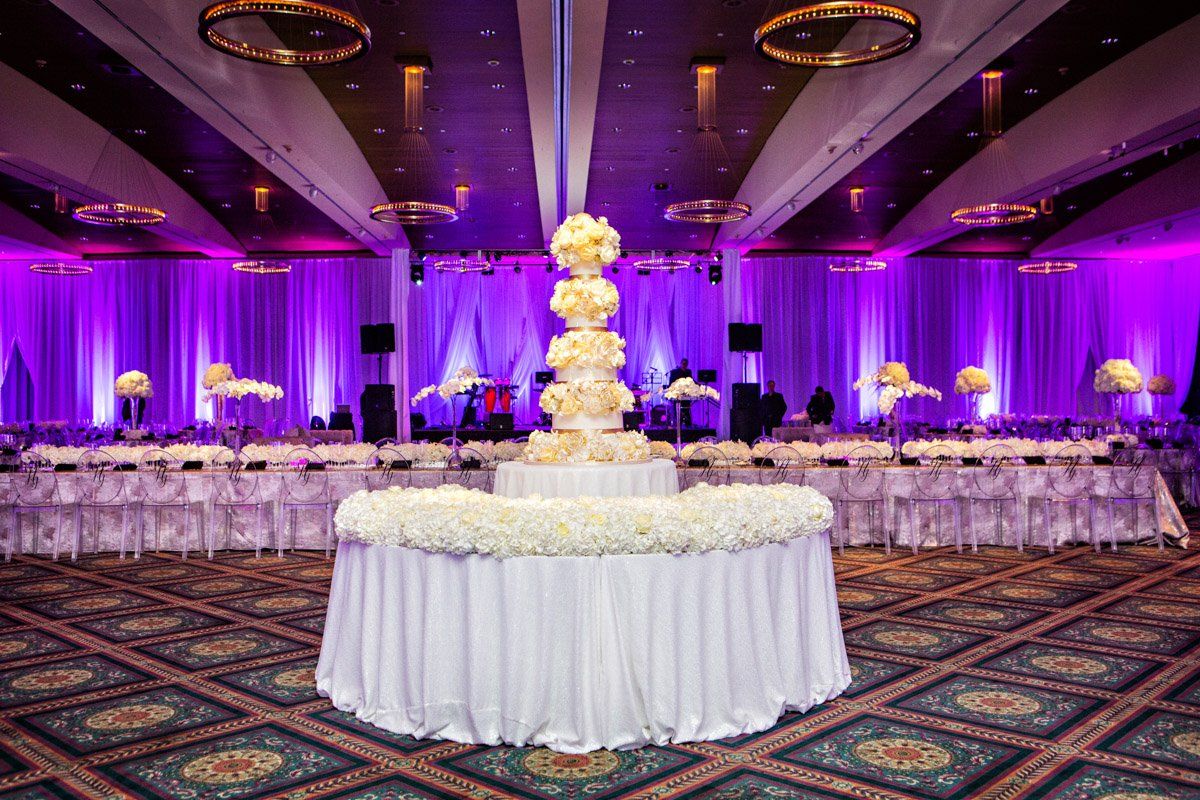 Wedding reception hall with purple uplighting, floral centerpieces, and a multi-tiered cake.