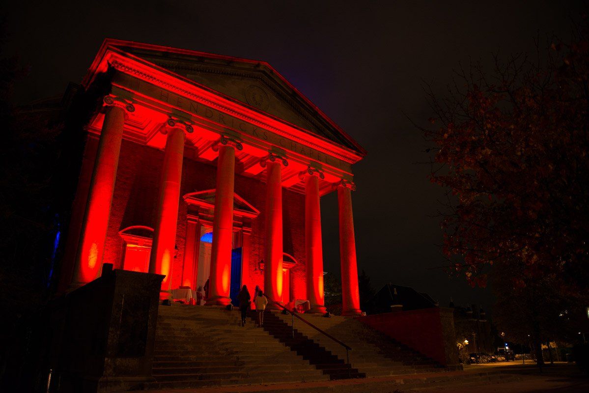 Red-lit classical building at night; columns, steps, a few people visible.