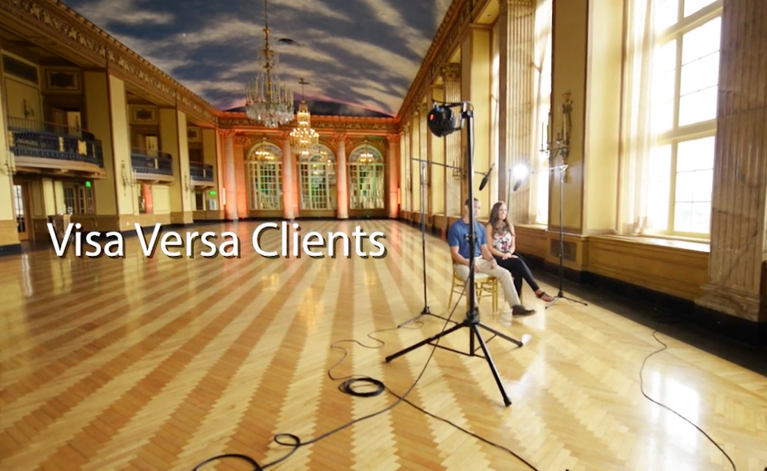 Two people being interviewed in a large room with wood floors, elegant architecture, and a sky-painted ceiling.