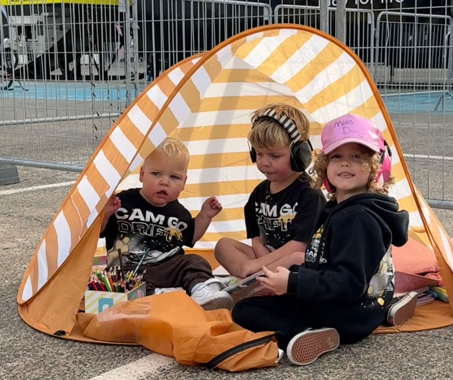 Three children are sitting in an orange and white striped tent.