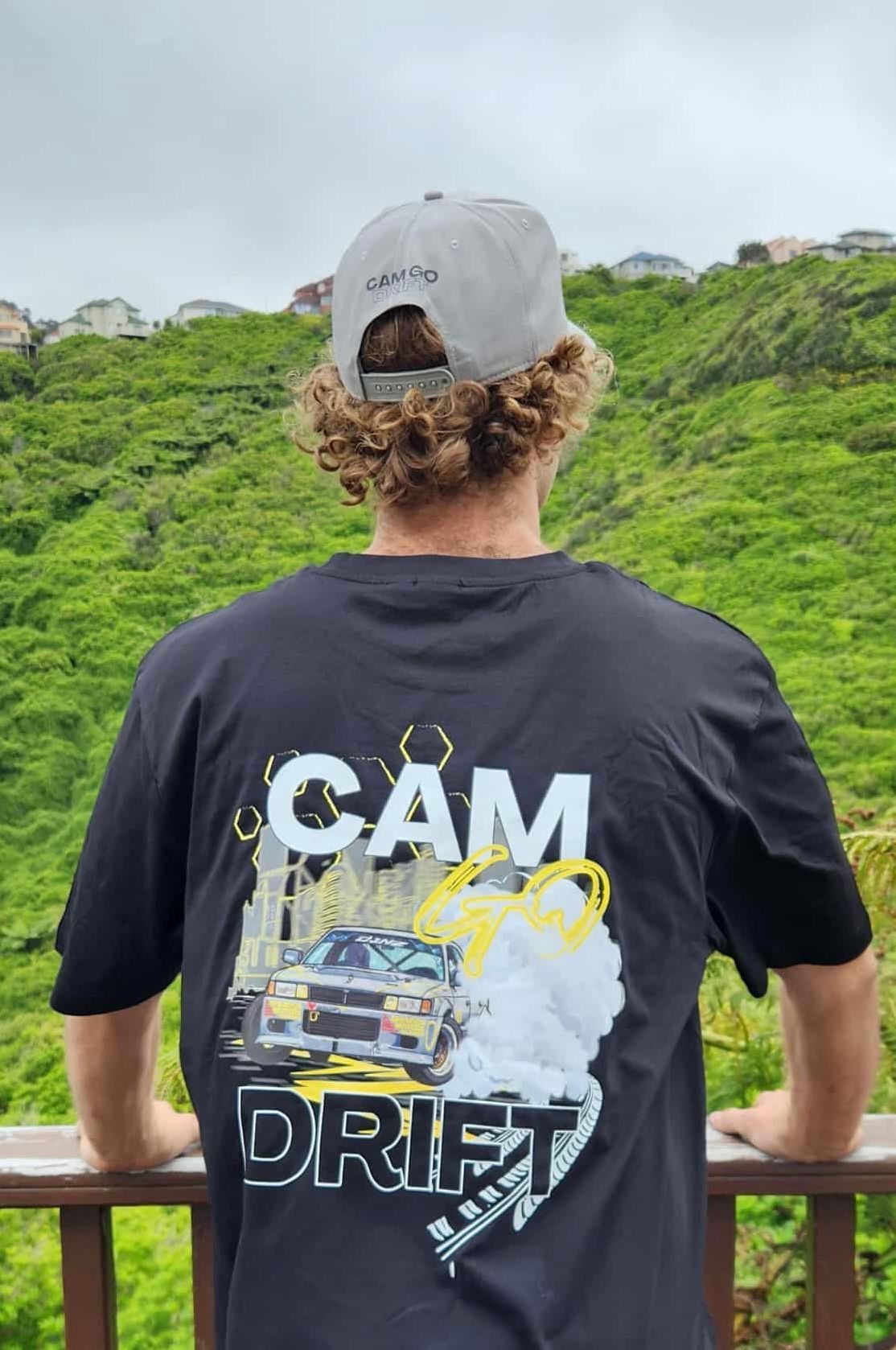 Boy in gray hat and black shirt with graphic, touching cap, outdoors.