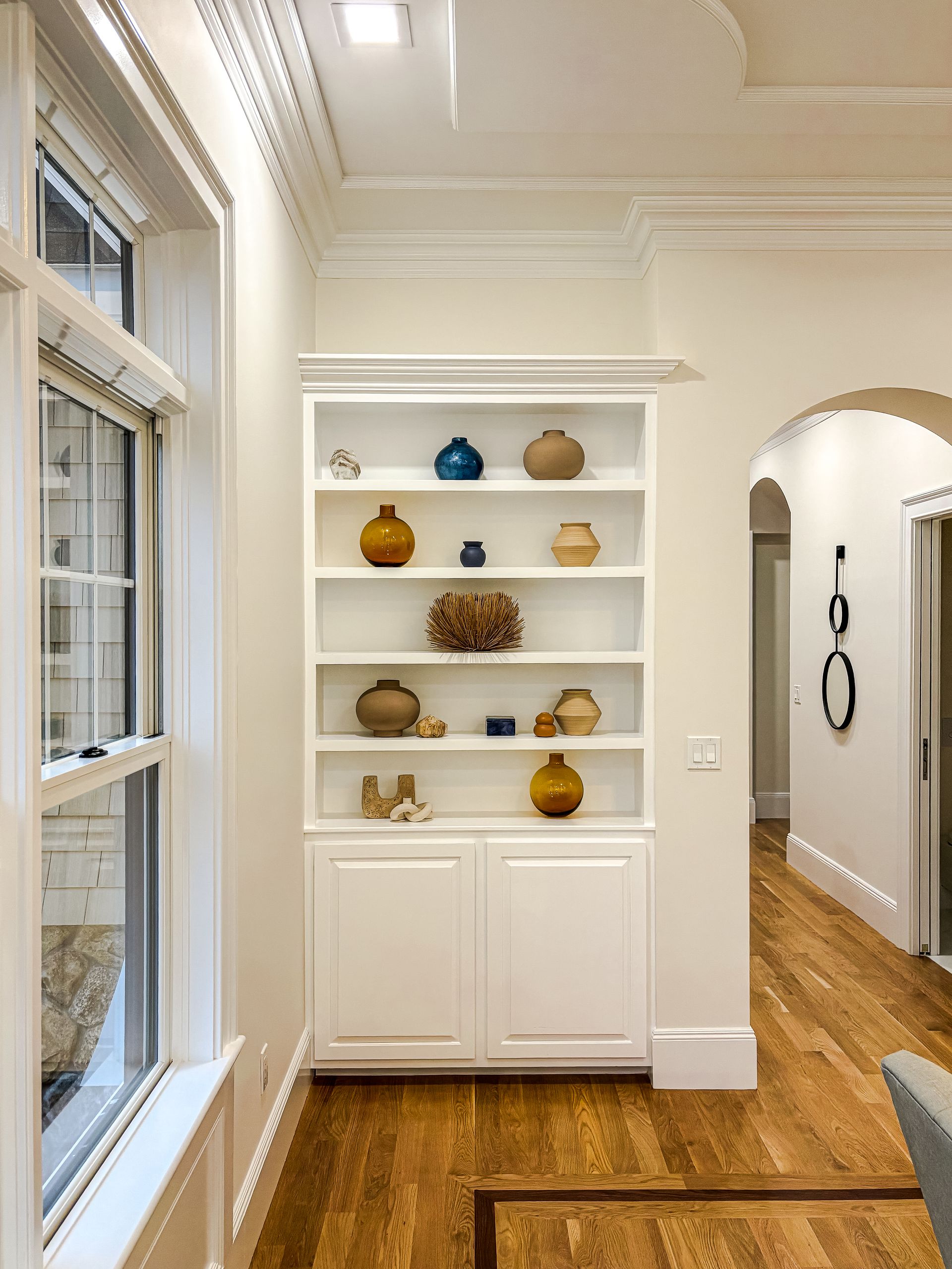 A white bookshelf with vases on it in a living room next to a window.