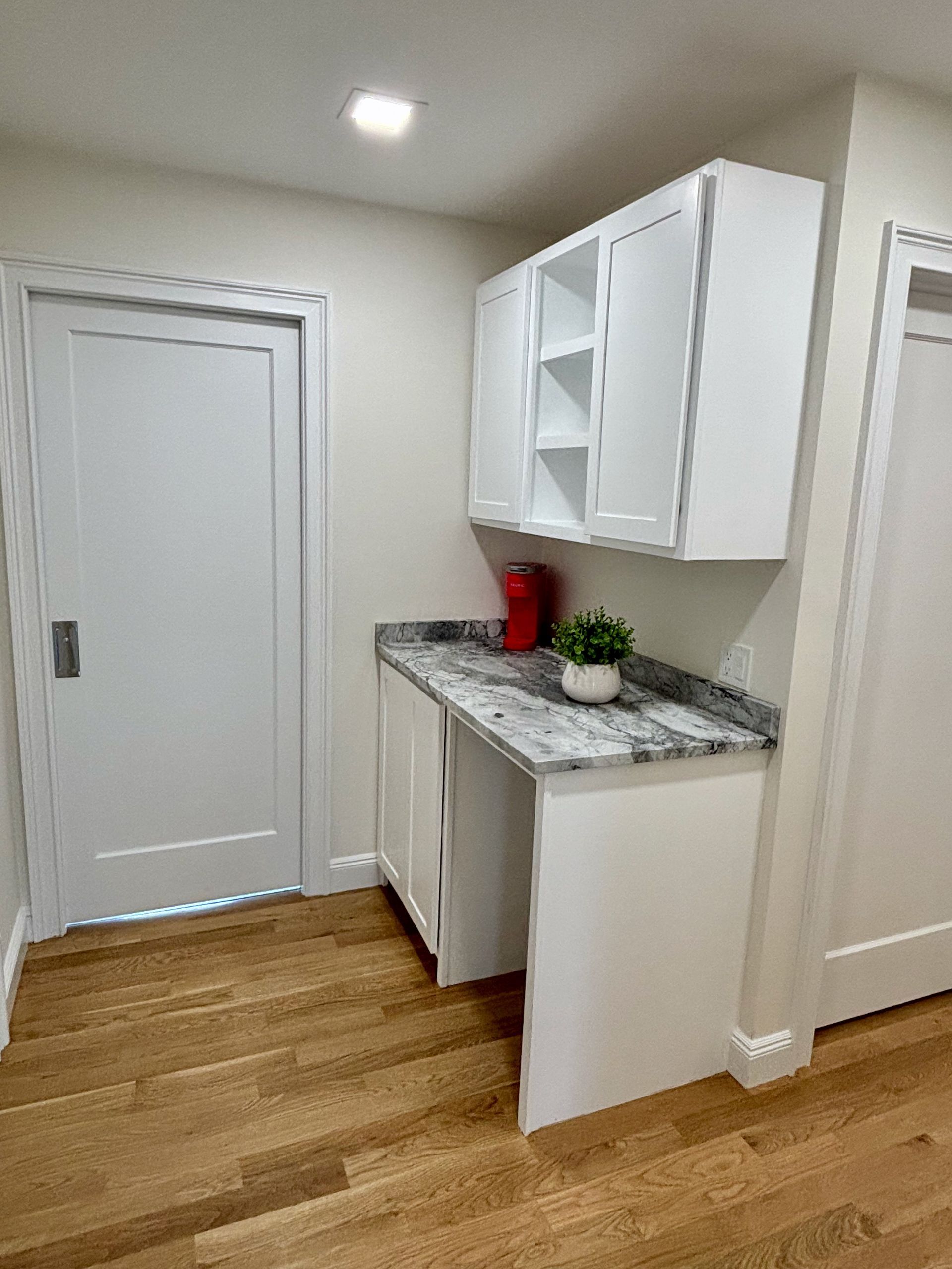 A kitchen with white cabinets , granite counter tops , and hardwood floors.