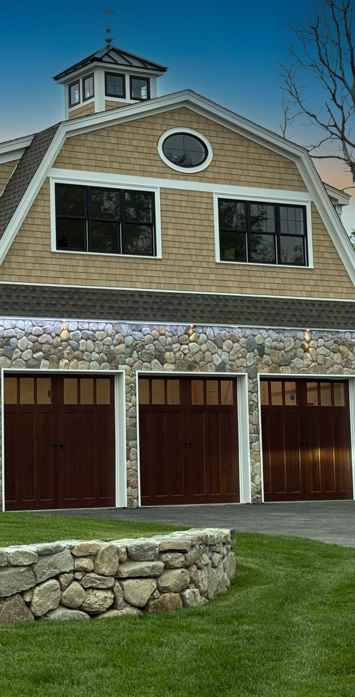 A large house with three garage doors and a stone wall in front of it.
