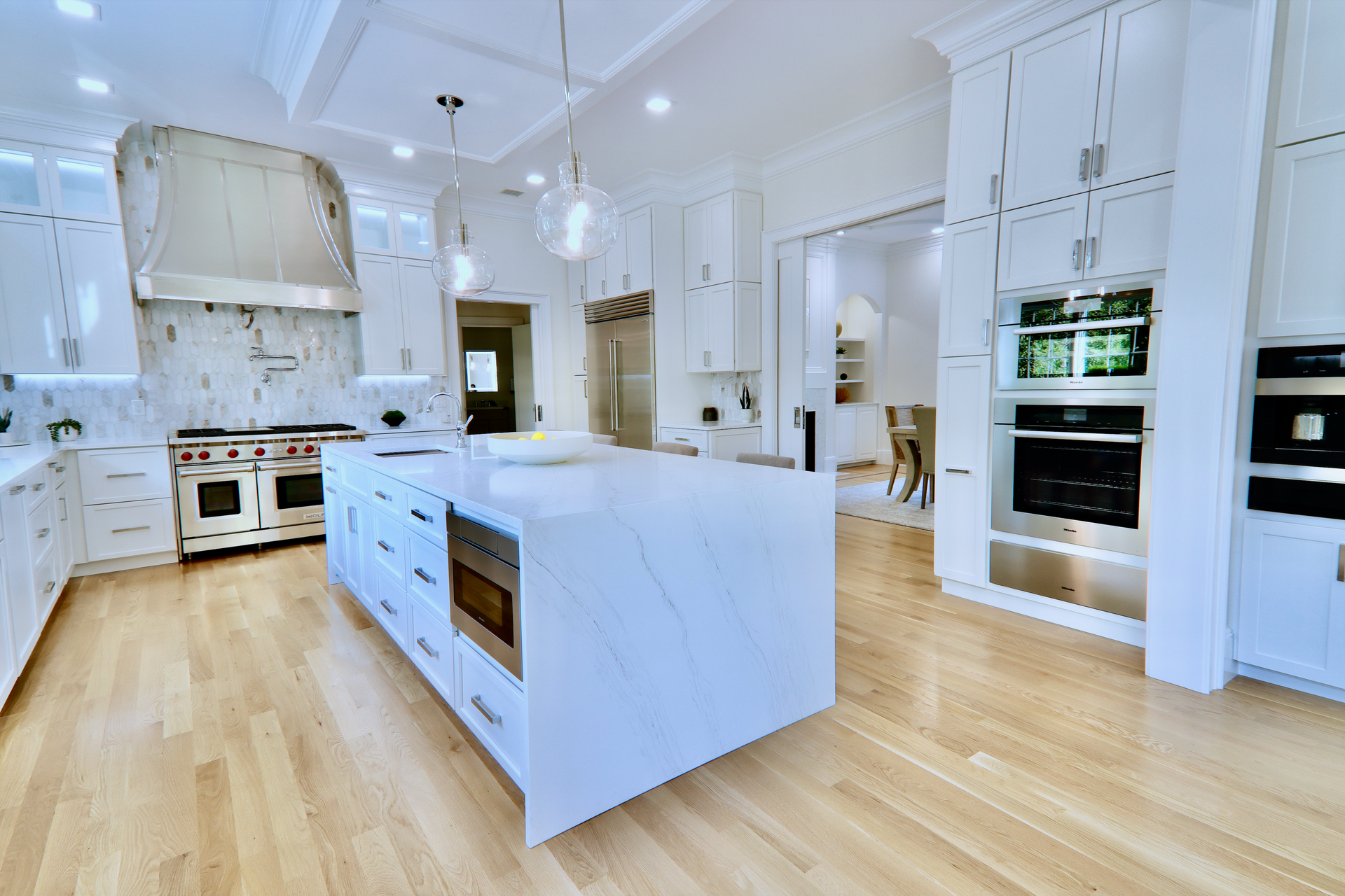 A long kitchen with white cabinets and hardwood floors.