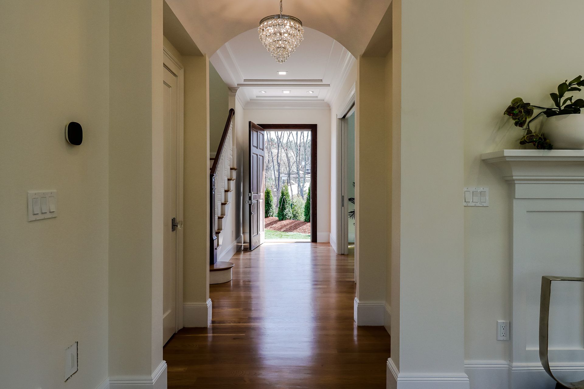 A hallway in a house with hardwood floors and a chandelier hanging from the ceiling.