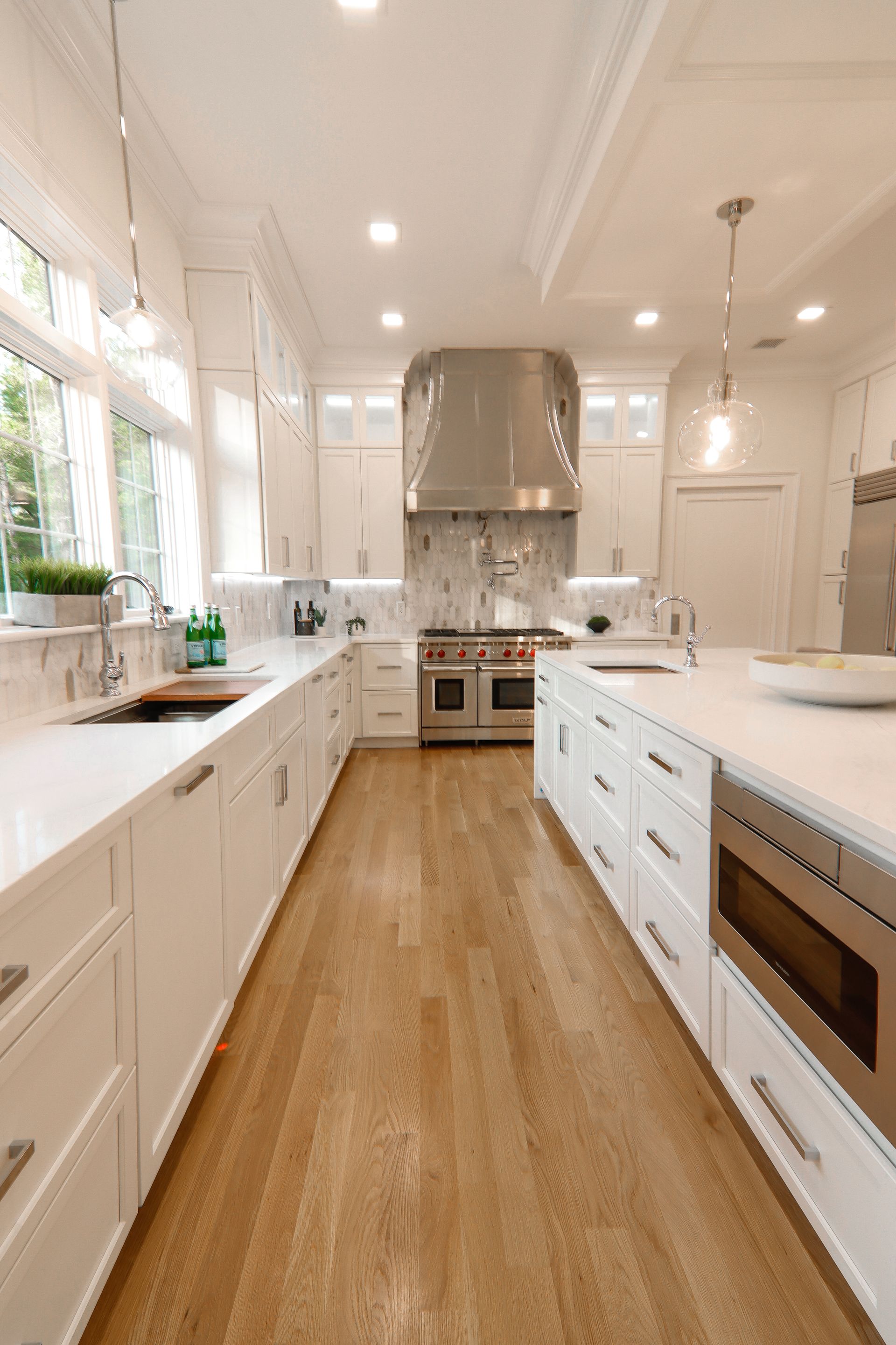 A long kitchen with white cabinets and hardwood floors.