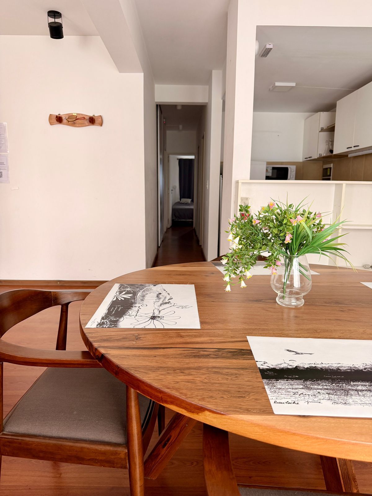 Mesa de comedor con cubiertos, flores y un pasillo que conduce a un dormitorio.