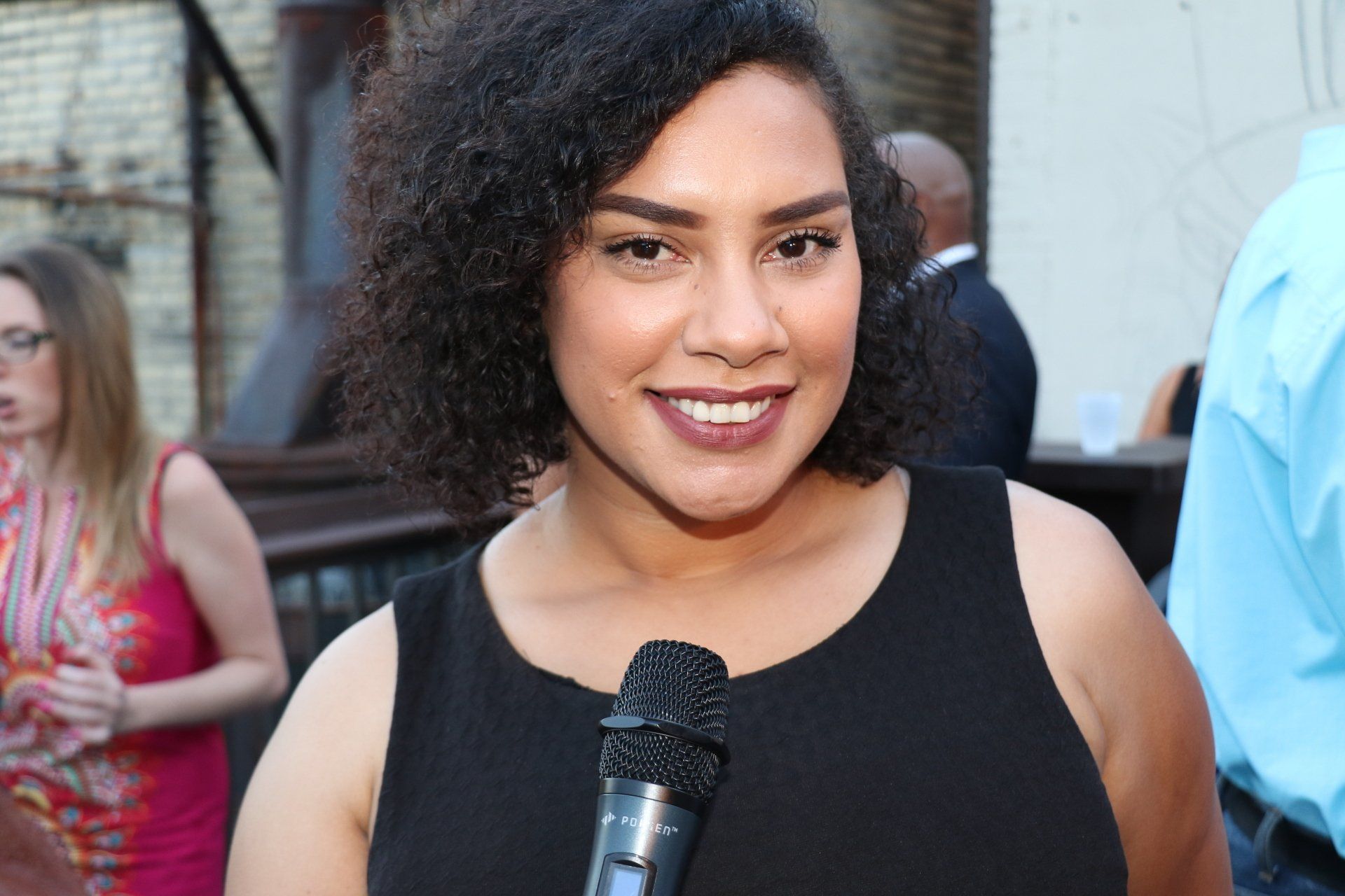 A woman in a black dress is holding a microphone and smiling.