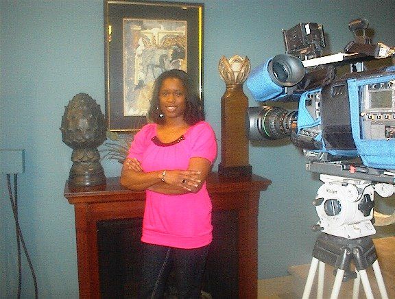 A woman in a pink shirt stands in front of a camera